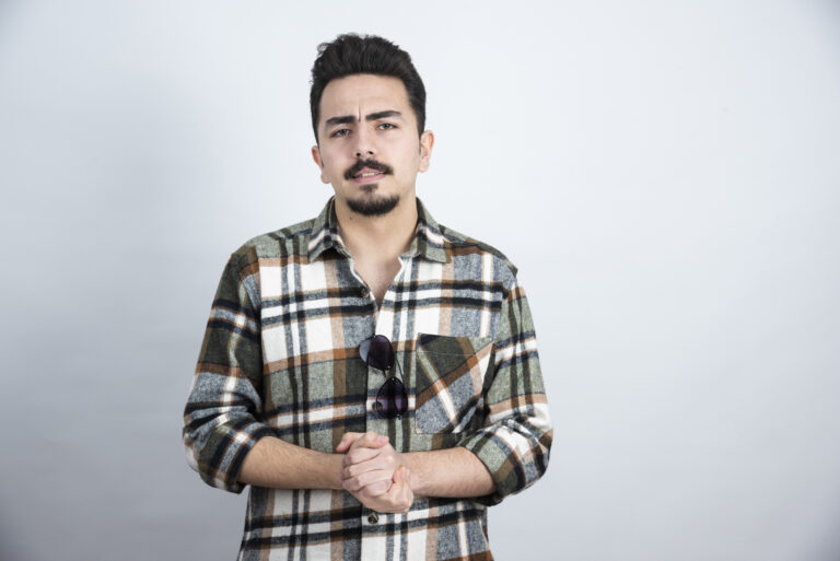 Portrait of bearded man with glasses standing over white wall